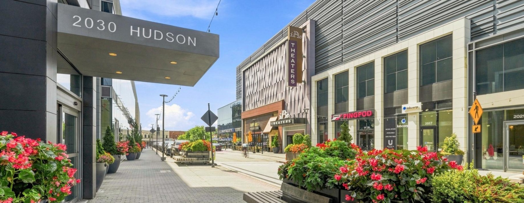 Sideway view of apartment building entrance showing 2030 Hudson and outdoor seating with flowers.